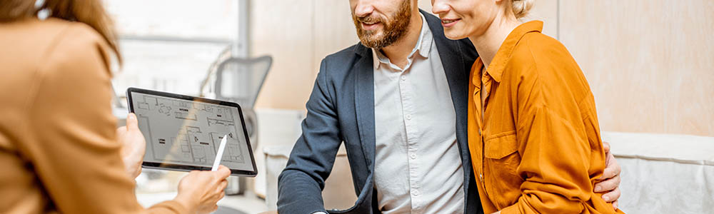 Young and lovely couple choosing a new house to buy, looking on the projects with a sales manager in the office of real estate agency