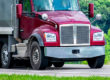 Large red dump trucking driving down a local road