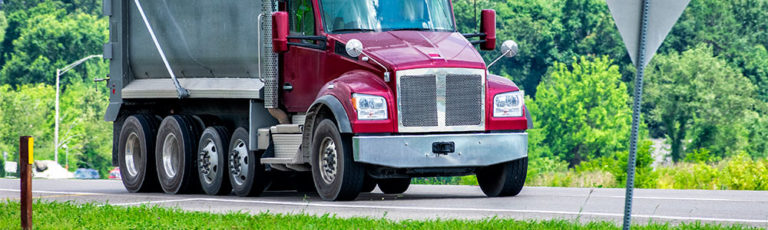 Large red dump trucking driving down a local road