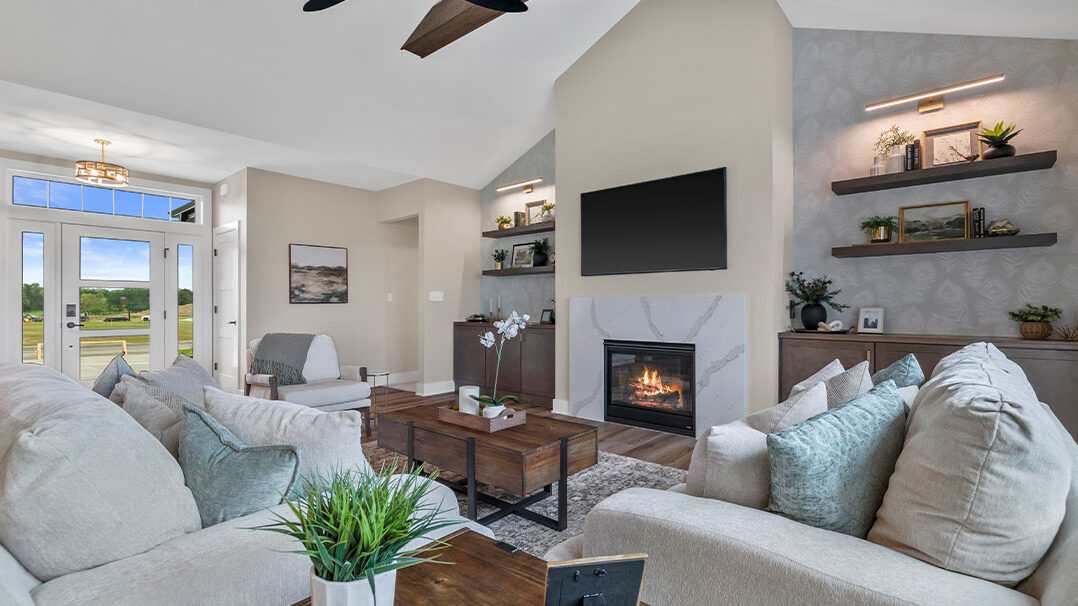 Parade of Homes model, The Lexi, great room with large grey couches and welcoming warm fireplace. Featuring two built-in with showcase personal items