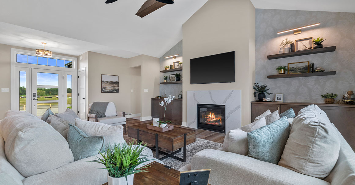 Parade of Homes model, The Lexi, great room with large grey couches and welcoming warm fireplace. Featuring two built-in with showcase personal items