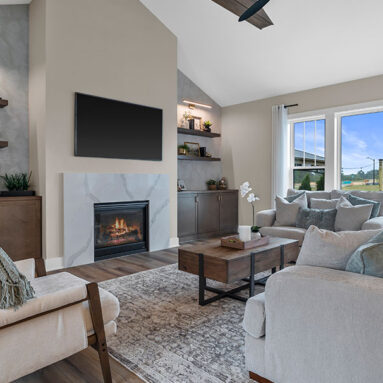 Parade of Homes model, The Lexi, great room with large grey couches and welcoming warm fireplace. Featuring two built-in with showcase personal items