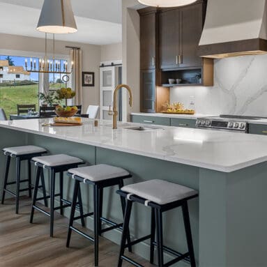 Parade of Homes model, The Lexi, kitchen featuring bright white counter tops, dark green grey lowers, and wood uppers. All the fine details feature bright gold.