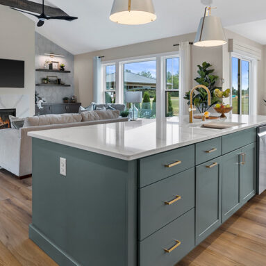 Parade of Homes model, The Lexi, kitchen featuring bright white counter tops, dark green grey lowers, and wood uppers. This angle looks at the great room.