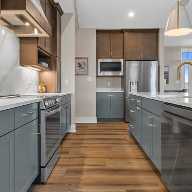 Parade of Homes model, The Lexi, kitchen featuring bright white counter tops, dark green grey lowers, and wood uppers. All the fine details feature bright gold.