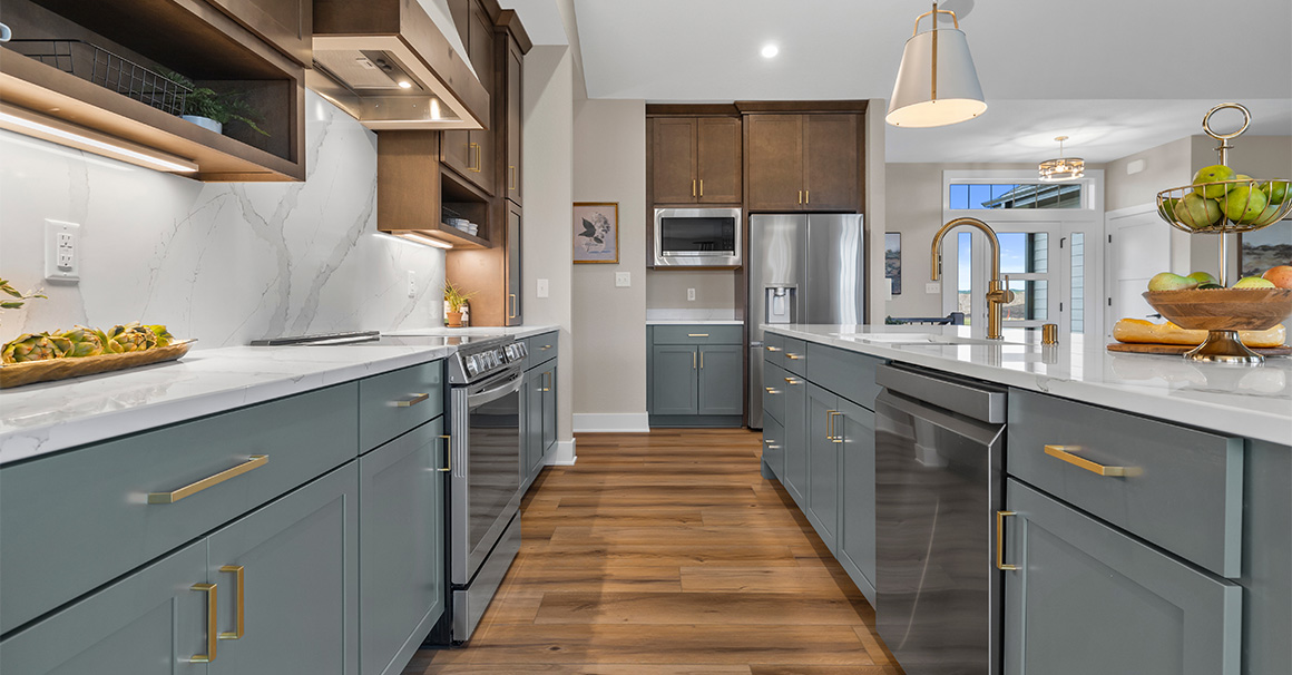 Parade of Homes model, The Lexi, kitchen featuring bright white counter tops, dark green grey lowers, and wood uppers. All the fine details feature bright gold.